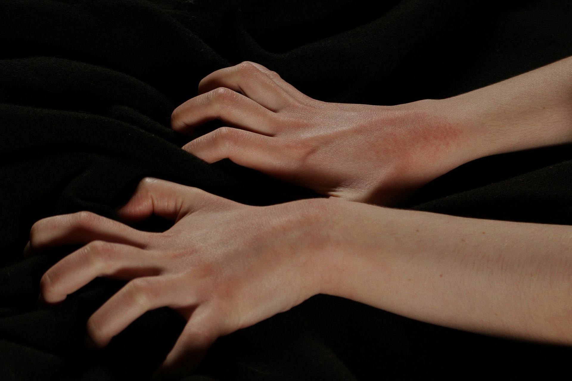 Deux mains agrippant un drapé de tissu noir, peau éclairée sur fond obscur